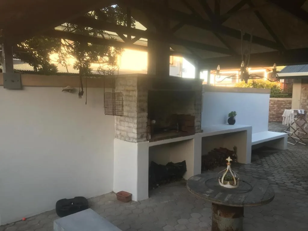 Outdoor braai area with fireplace and seating under pergola at sunset