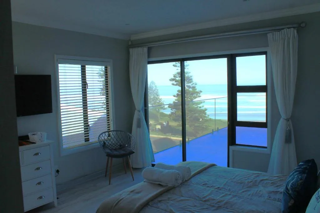 Bedroom with ocean view through glass doors and windows overlooking coast