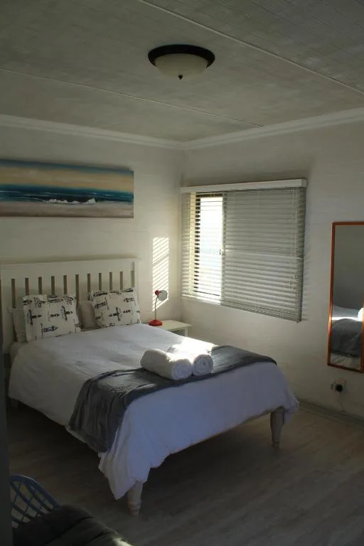 Bright bedroom with white bed, rolled towels, and ocean artwork on wall