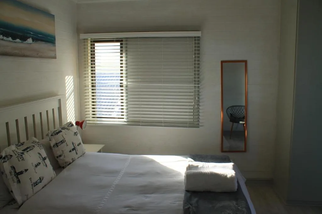 Bright bedroom with white bedding and ocean view through venetian blinds