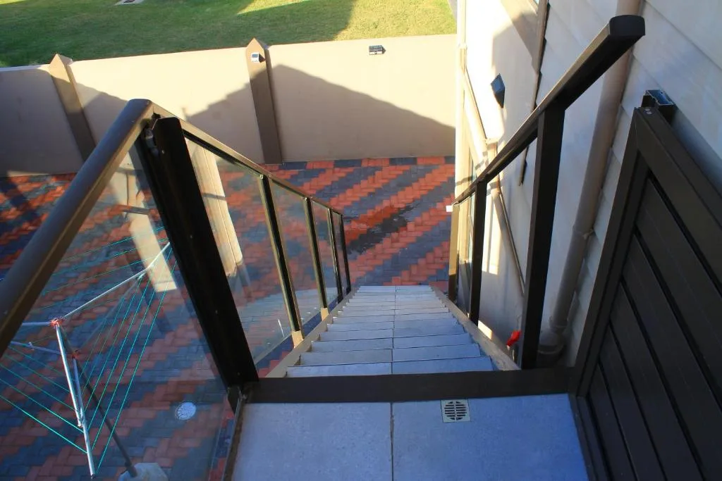 Outdoor deck with geometric patterned tiles and black railings overlooking lawn