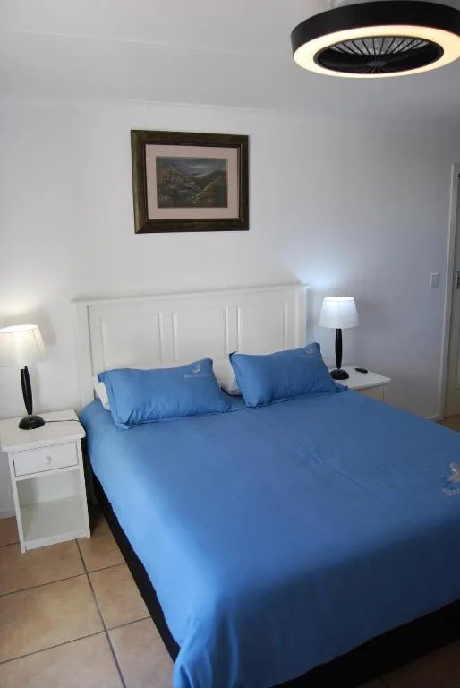 Bright bedroom with blue bedding, white headboard, and framed landscape artwork