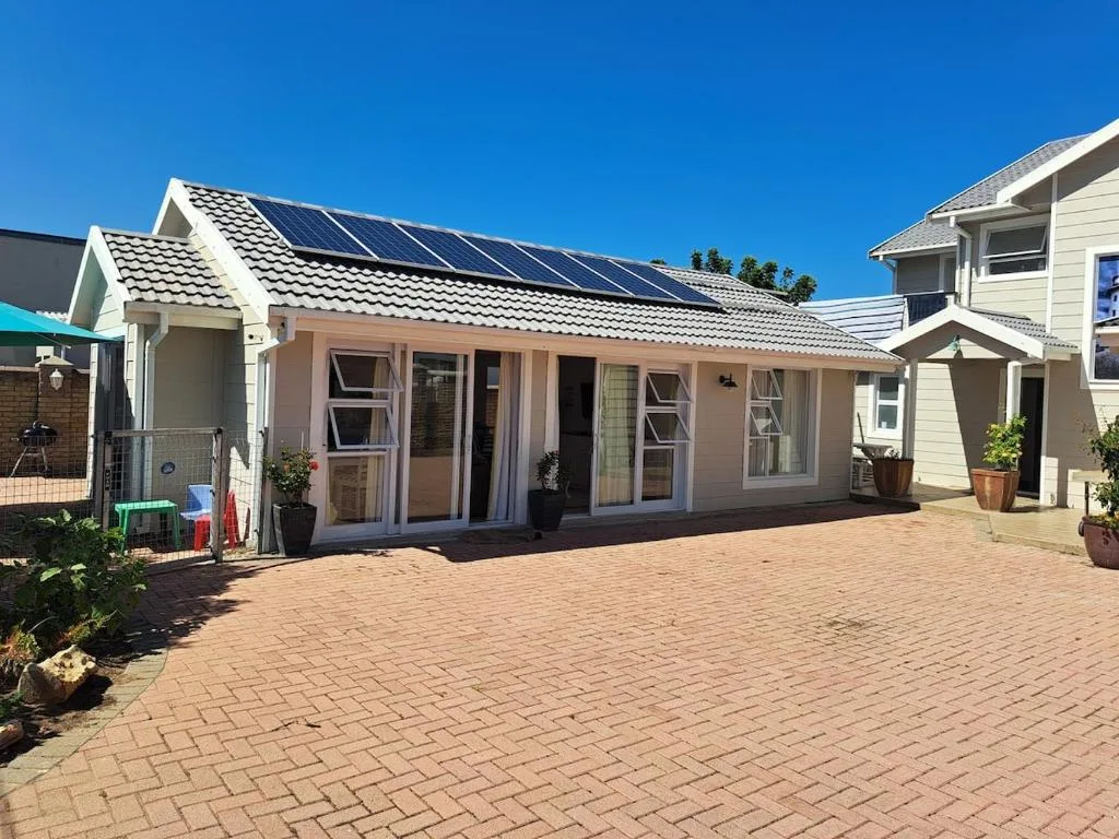 Beige cottage with solar panels, brick patio, and clear blue sky