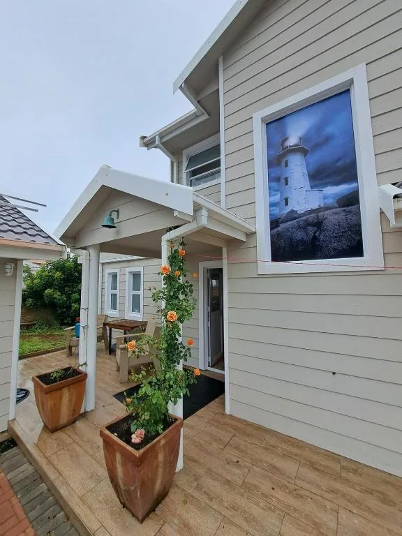Modern cottage entrance with flowering plants and lighthouse artwork on wall