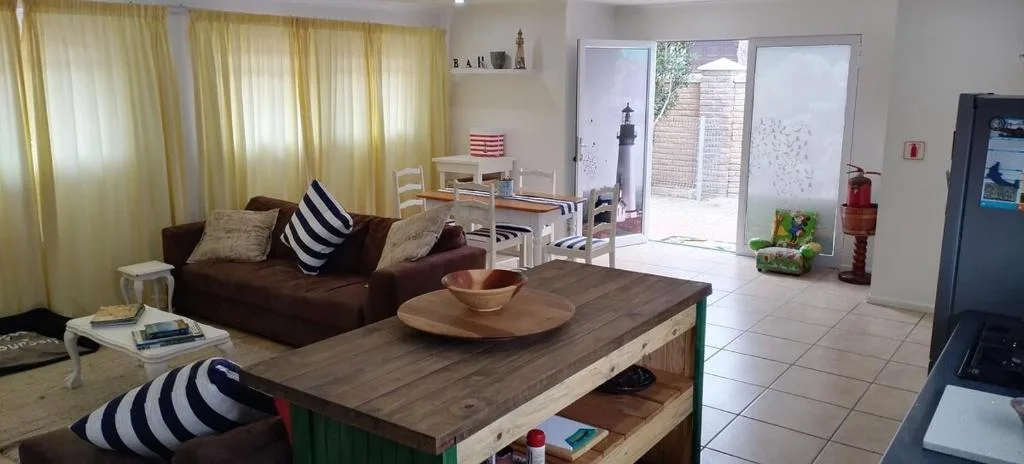 Spacious open-plan lounge with brown sofa, wooden coffee table, and bright windows