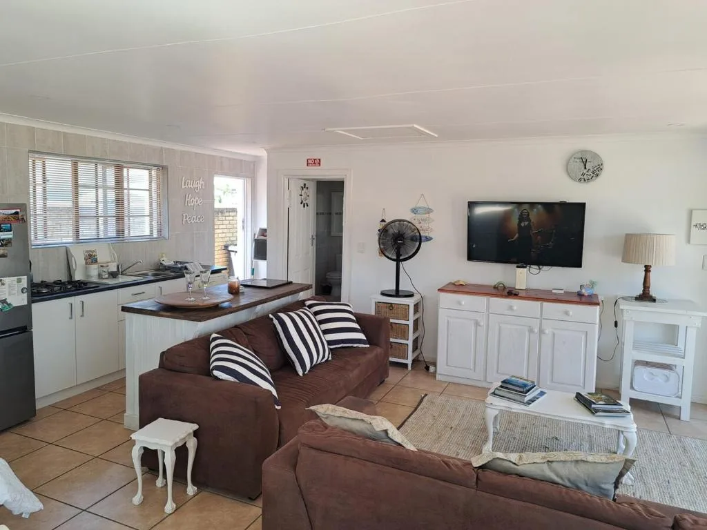 Open-plan living room with brown sofa, TV, and kitchen area visible