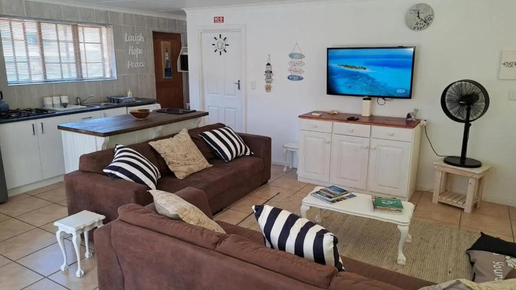 Open-plan lounge with brown sofas, TV, and kitchen visible in background