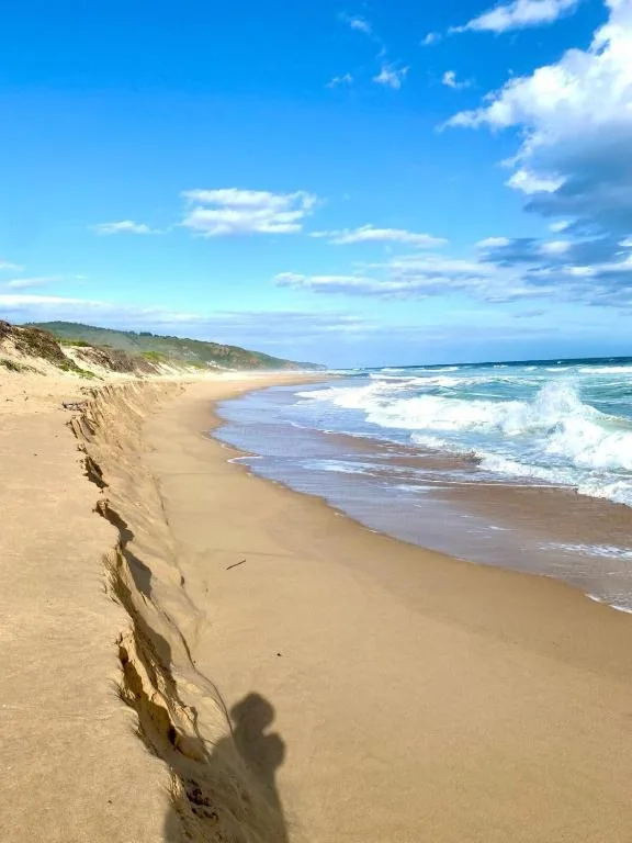 Wide sandy beach with rolling waves and dune cliffs along coastline
