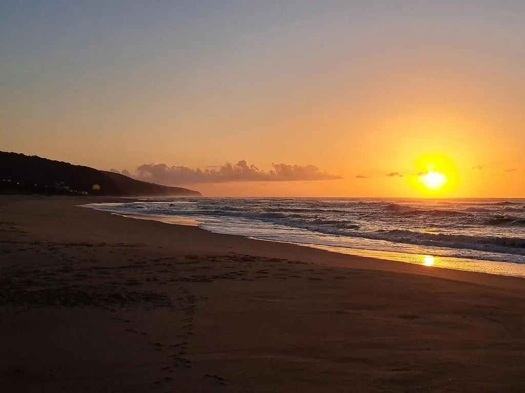 Golden sunset over ocean beach with waves and coastal cliffs