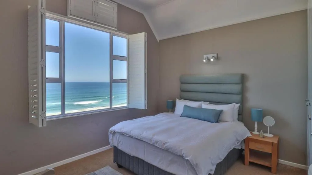 Bedroom with ocean view through large windows, bed with blue headboard