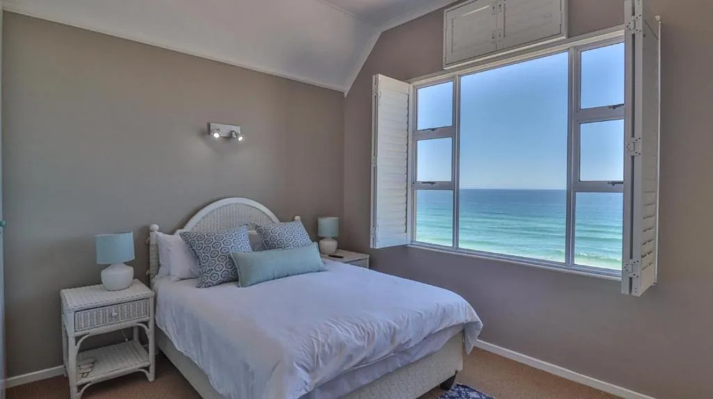Bedroom with ocean view through large windows and coastal furnishings
