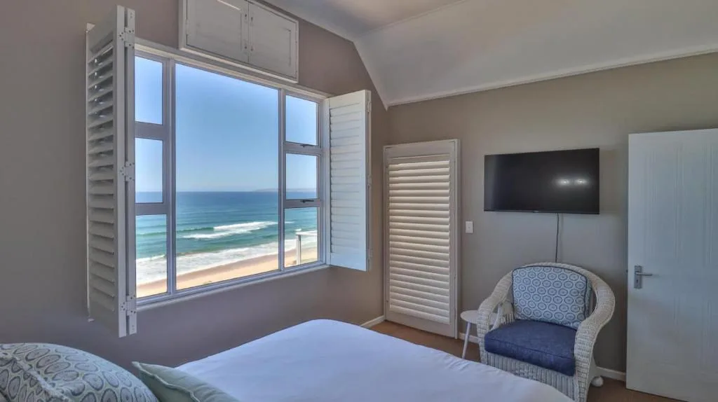 Bedroom with ocean view through large windows and mounted TV