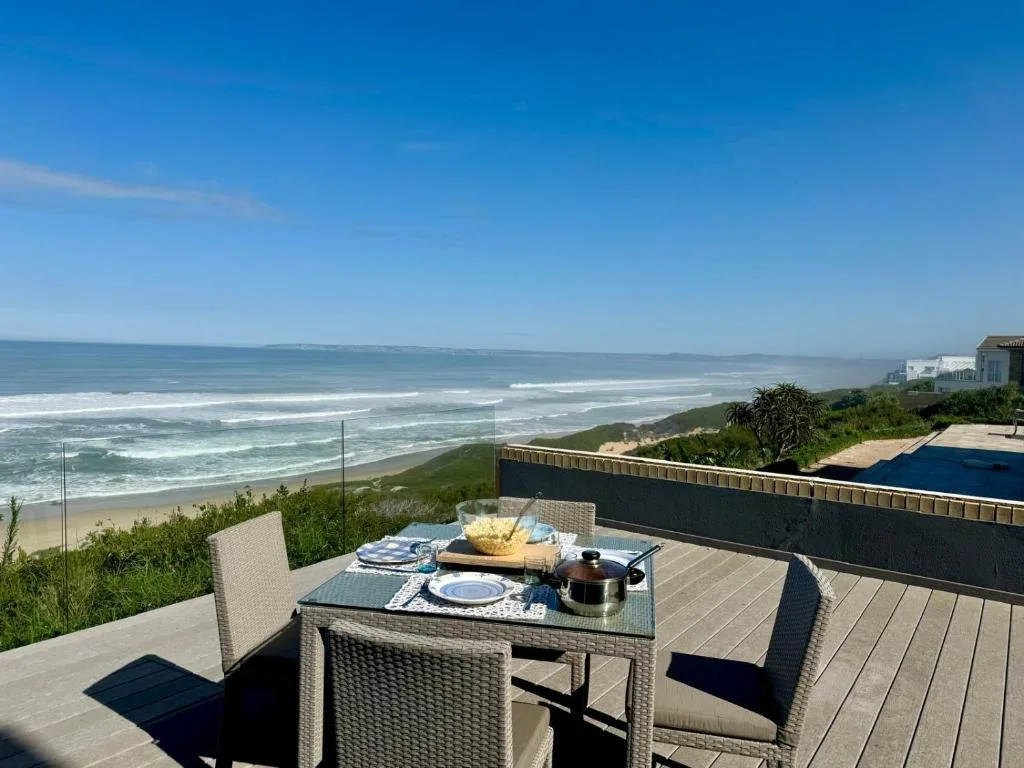 Outdoor dining table on wooden deck overlooking pristine beach and ocean