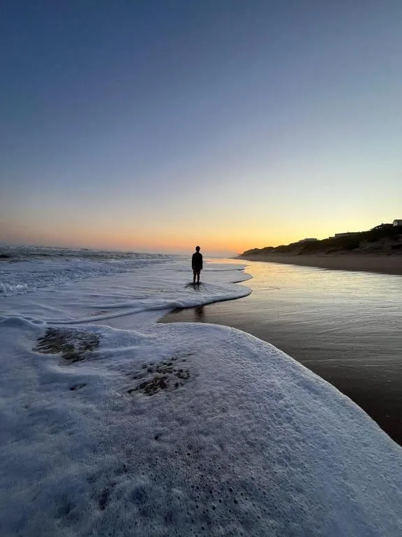Surfer standing in ocean at sunset with golden coastline and waves