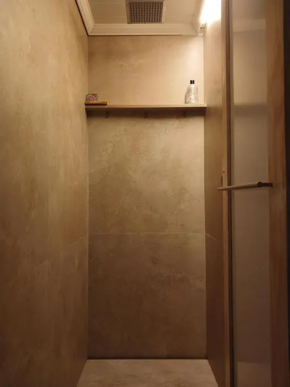 Minimalist shower enclosure with beige tiled walls and wooden shelf