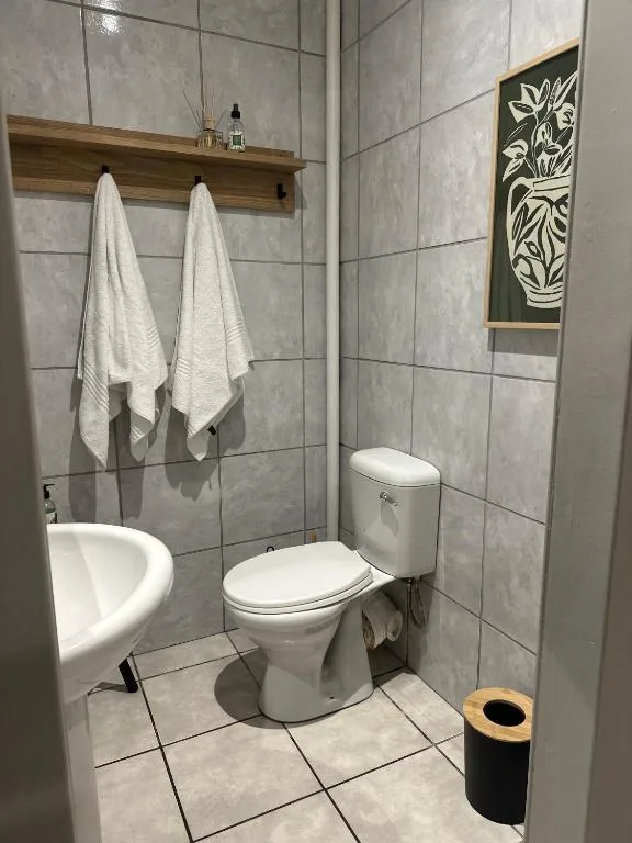 Modern bathroom with toilet, sink, and wooden shelf with white towels