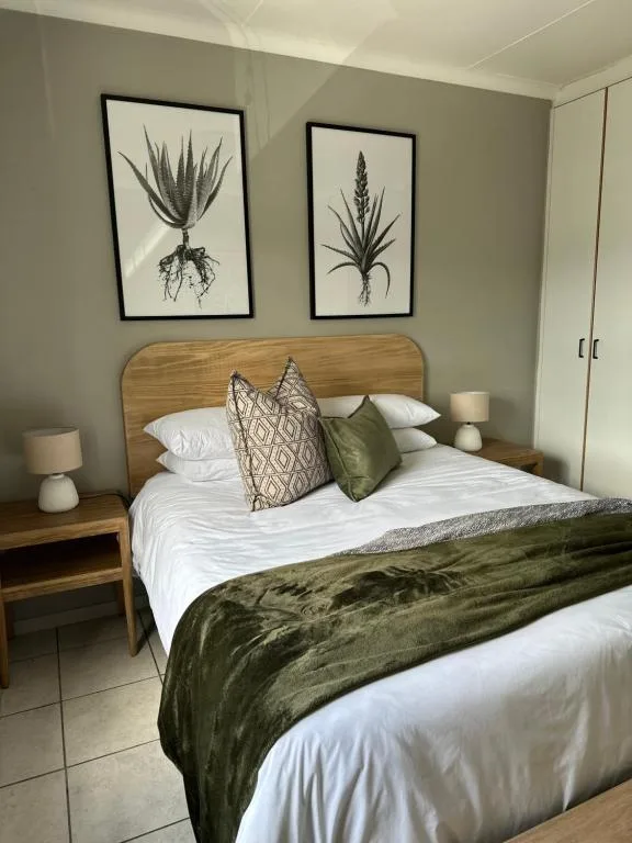 Modern bedroom with wooden bed frame, white bedding, and botanical wall art