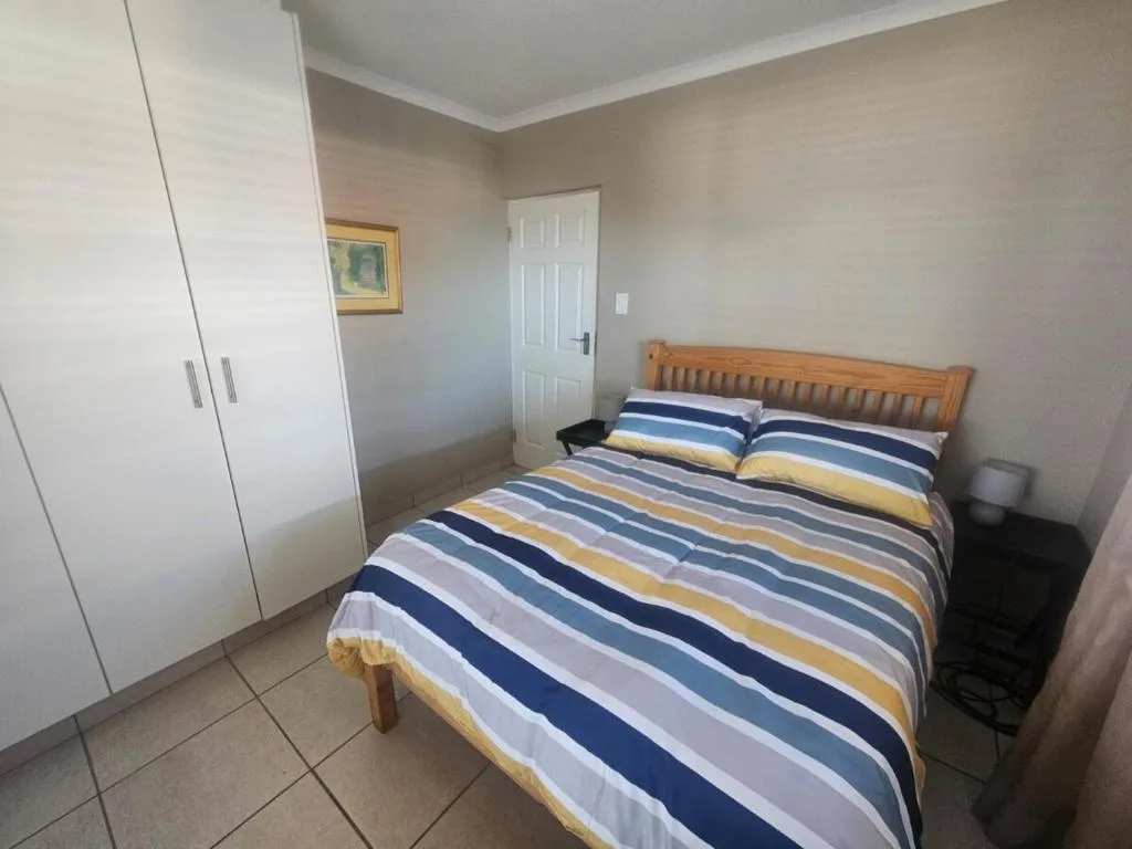 Bright bedroom with striped bedding, wooden headboard, and built-in wardrobe