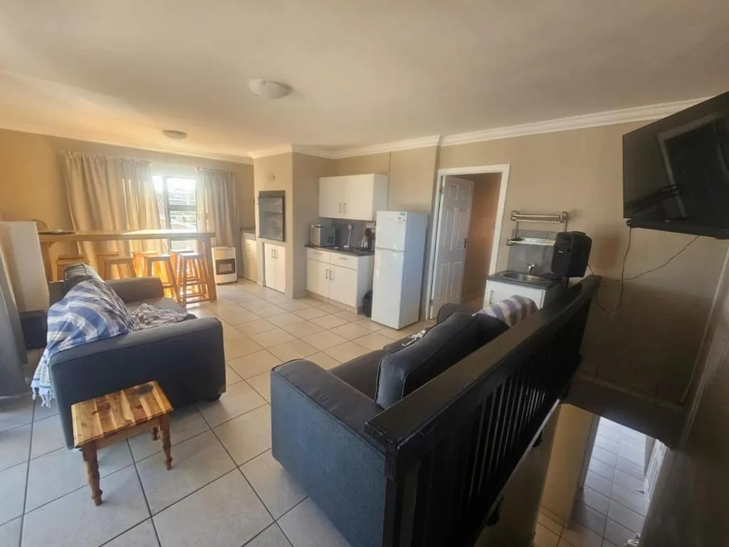 Open-plan lounge with dark sofas, TV, and kitchenette visible in background