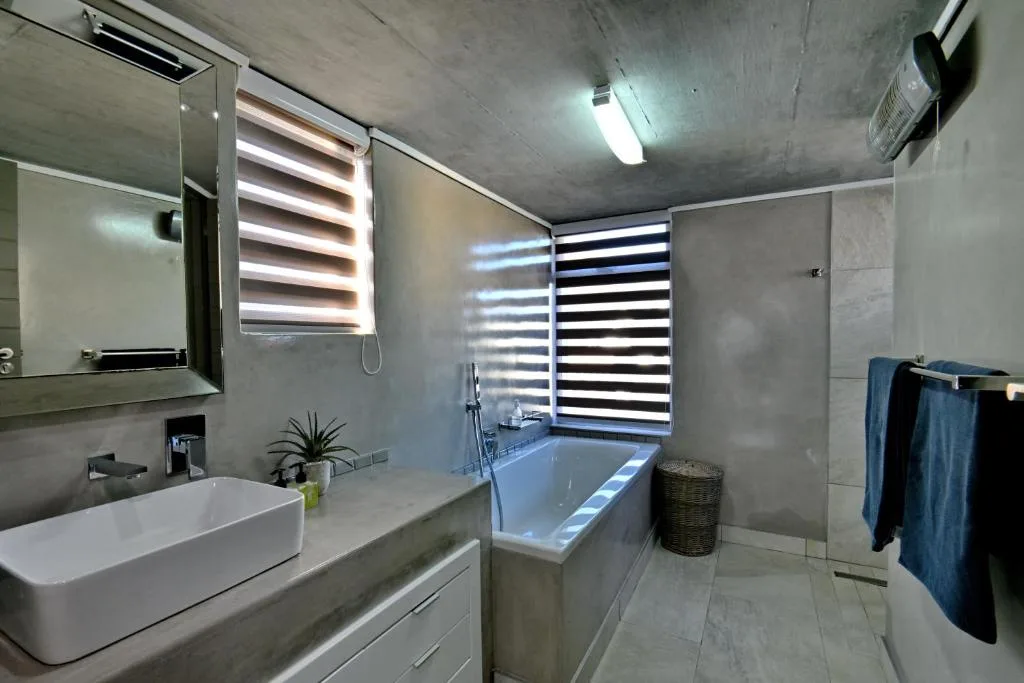 Modern bathroom with white vanity, bathtub, and striped roller blinds