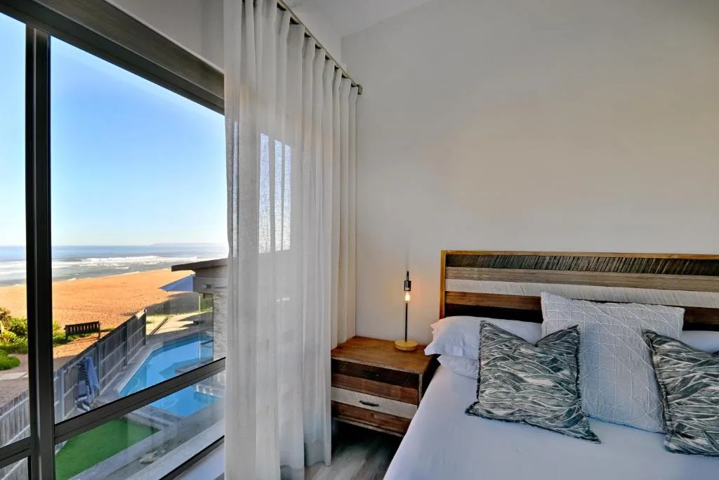 Bright bedroom with ocean view through floor-to-ceiling windows and pool below