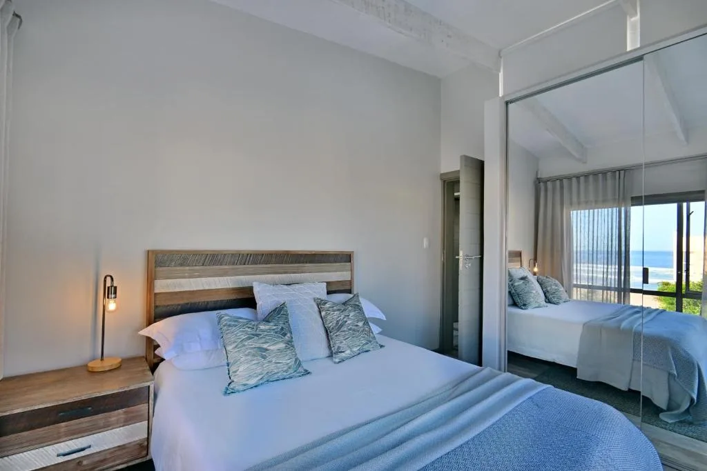 Modern bedroom with ocean view, wooden bed frame, and mirrored wardrobe doors