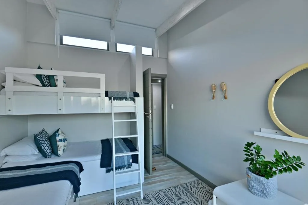 Modern bedroom with white bunk beds, round mirror, potted plant decoration