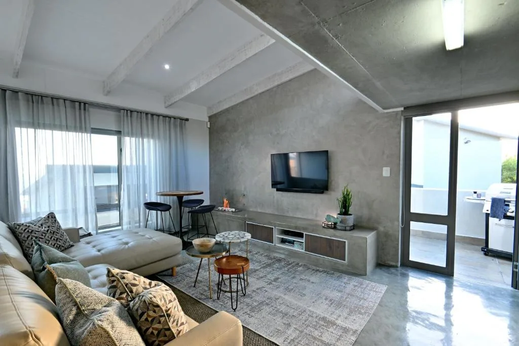 Modern lounge with sofa, TV wall, and ocean views through glass doors