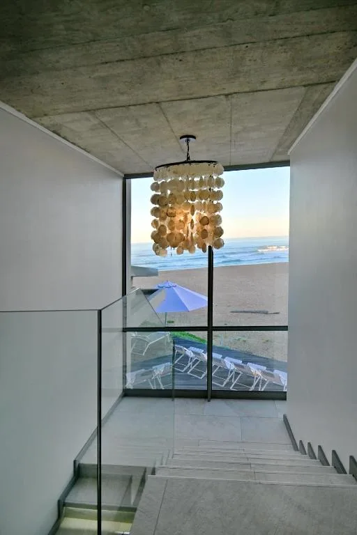 Beachfront vista through floor-to-ceiling windows, ocean and sandy shore visible