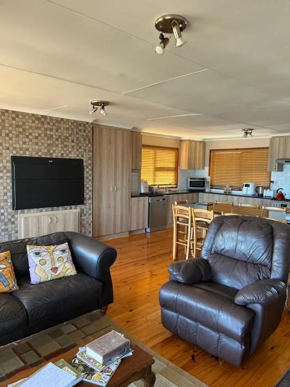 Open-plan lounge with black leather recliners, TV, and kitchen visible beyond