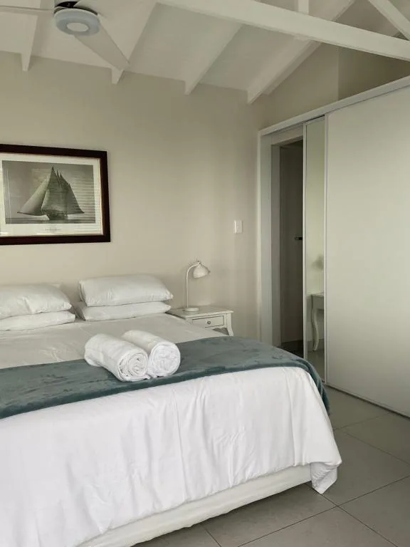 Bright bedroom with white bedding, rolled towels, and coastal artwork