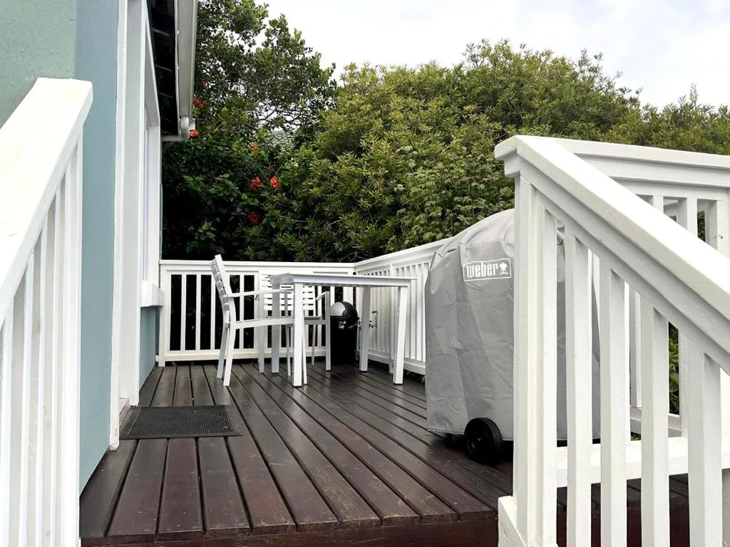 Spacious wooden deck with white railings, outdoor seating, and braai area