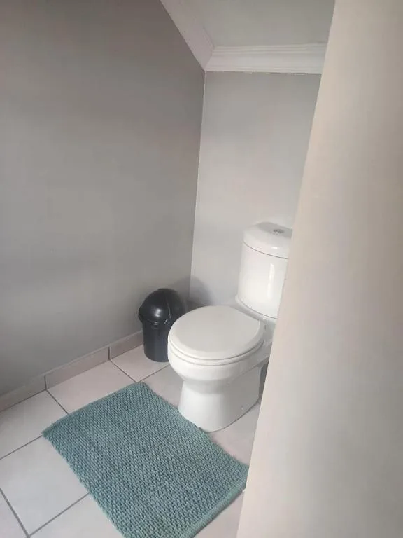 Clean white toilet in compact bathroom with teal mat