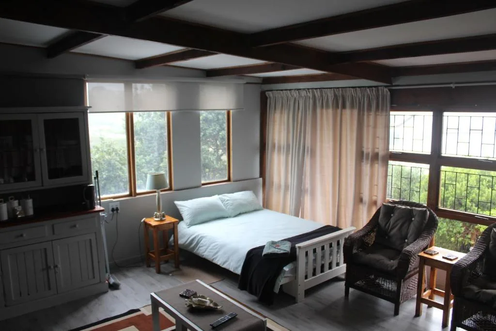 Spacious bedroom with queen bed, lounge seating, and large windows overlooking greenery