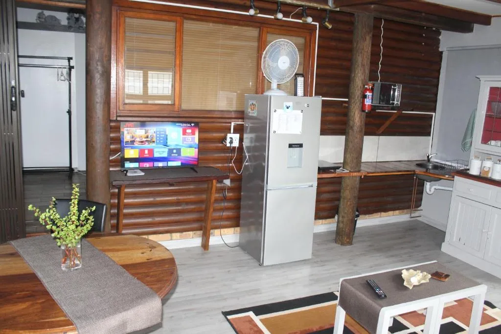 Open-plan lounge with TV, wooden beams, sofa seating, and kitchen visible