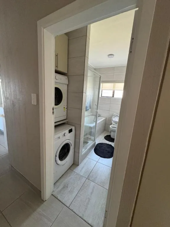 Bathroom with shower enclosure, toilet, and stacked washing machines