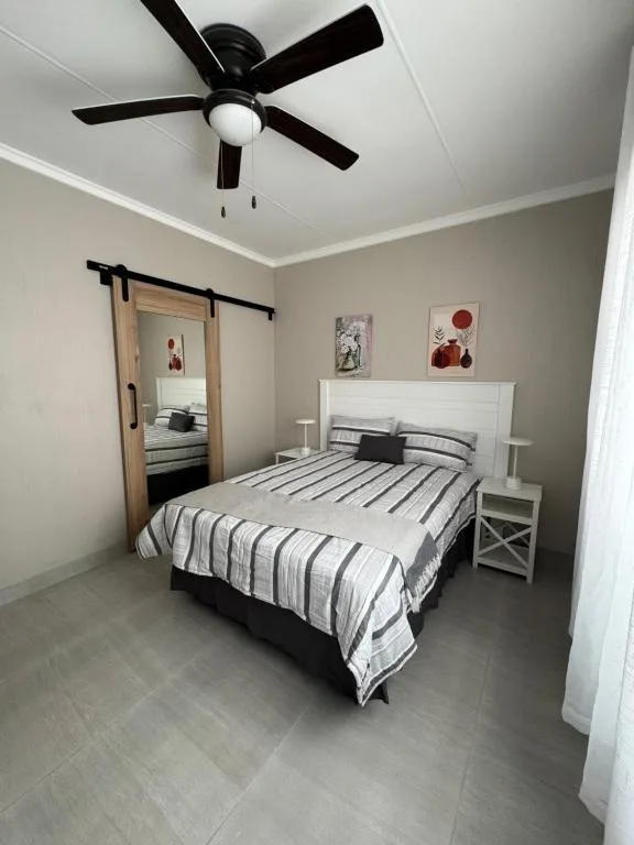 Modern bedroom with white bed frame and striped bedding, black ceiling fan