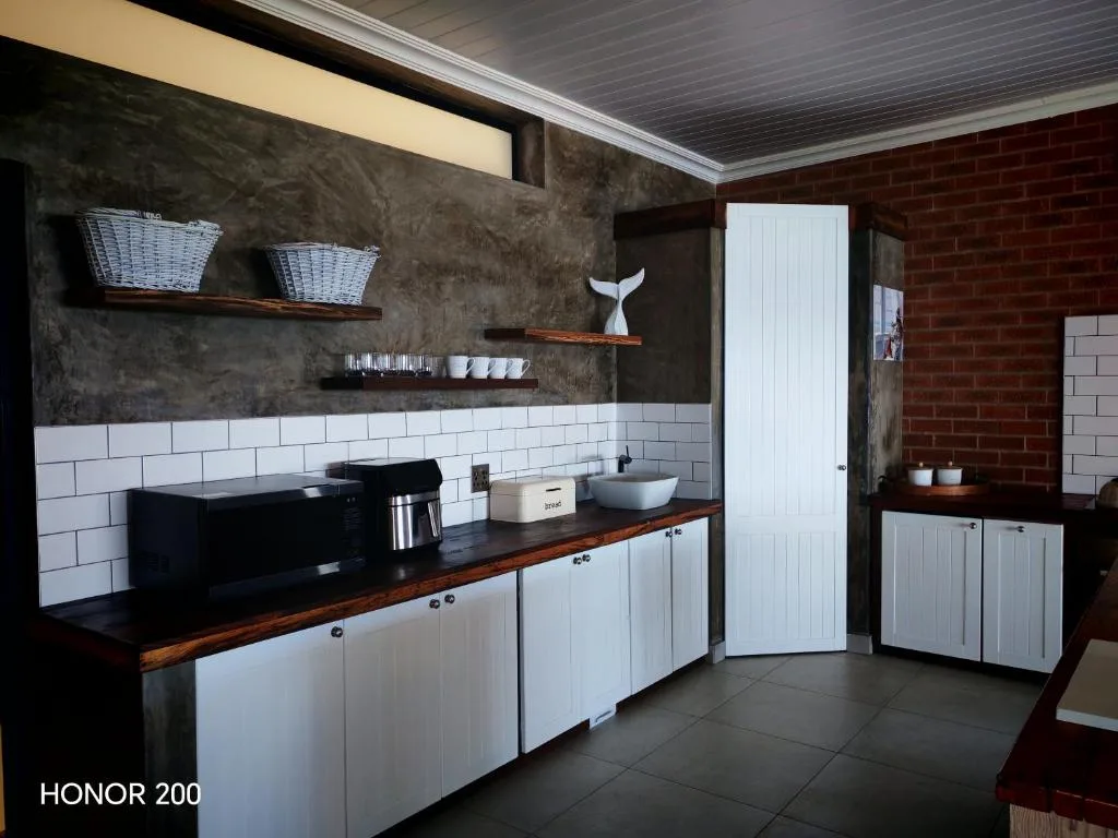 Modern kitchen with white cabinetry, black countertop, and open shelving with décor