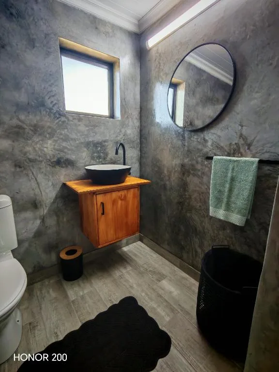 Modern bathroom with concrete walls, wooden vanity, round mirror, and window