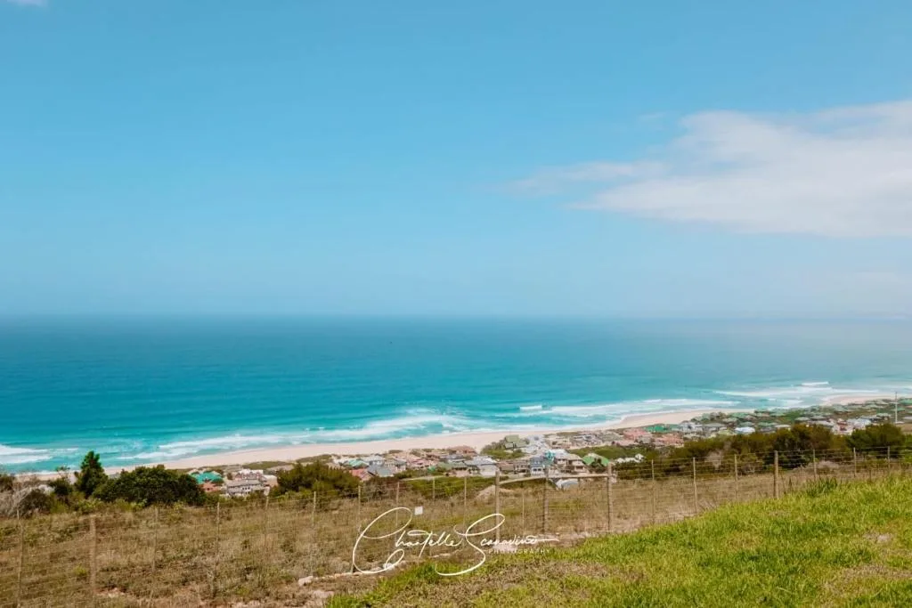 Expansive coastal view with turquoise ocean, white sand beach, and rolling hills