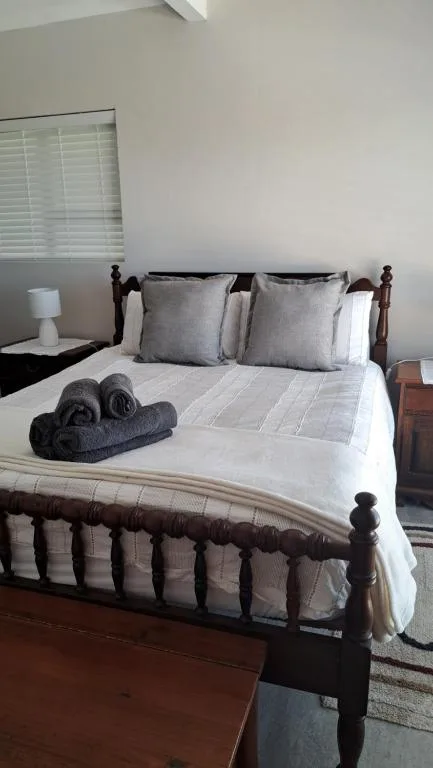 Neatly made bed with gray pillows and white linens, dark wood frame