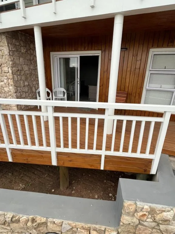 Covered wooden deck with white railings and stone exterior walls