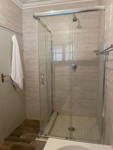 Modern glass-enclosed shower with beige tile walls and cream towel rack