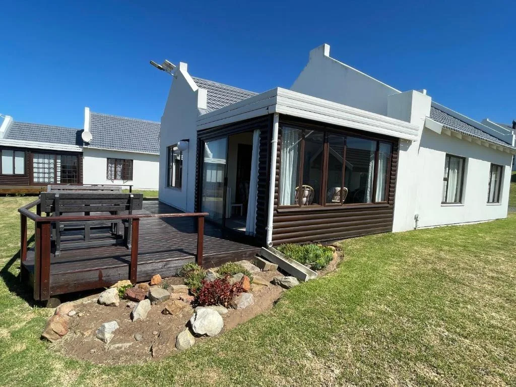 White coastal cottage with wooden deck and manicured garden landscaping