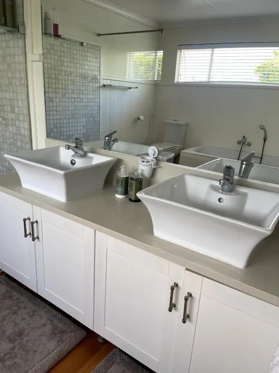Modern bathroom with dual white vessel sinks, grey tiled shower, and natural light