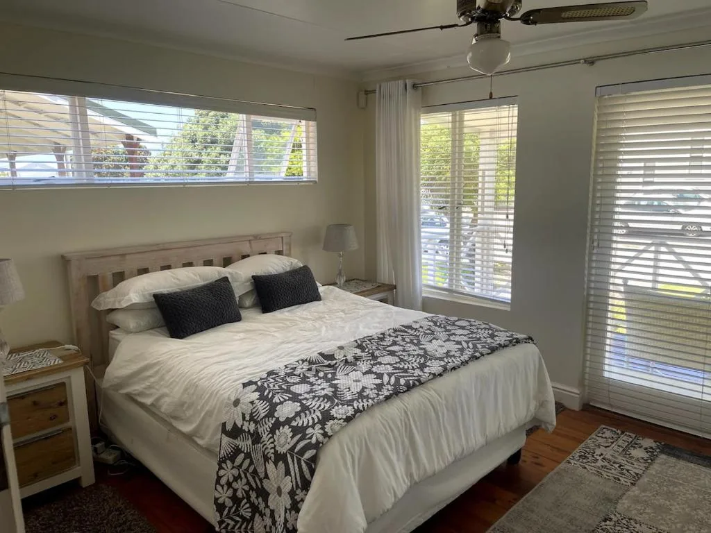 Bright bedroom with queen bed, white bedding, black patterned throw, and plantation shutters