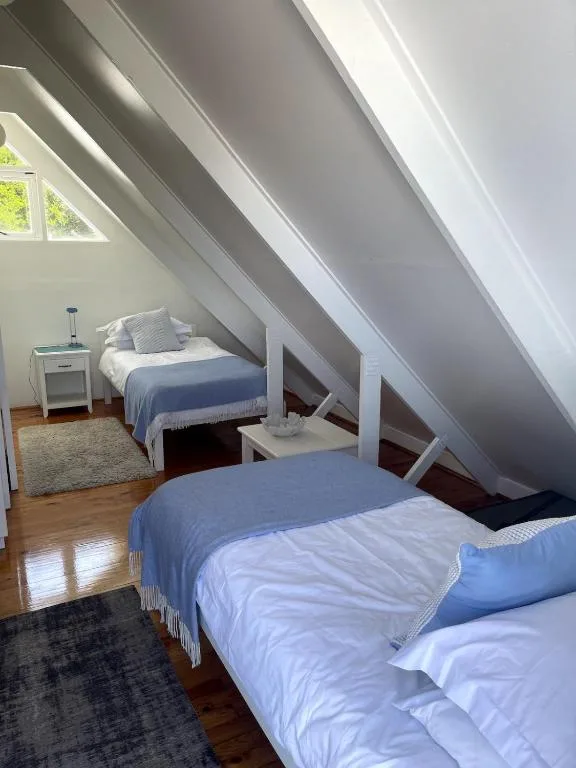 Bright attic bedroom with two beds and sloped white ceiling beams