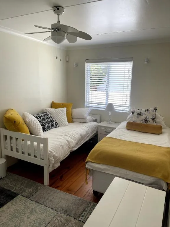 Bright bedroom with two single beds, yellow accents, and ceiling fan