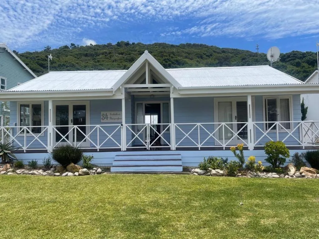 White cottage with wide front deck and manicured lawn surrounded by forested hills