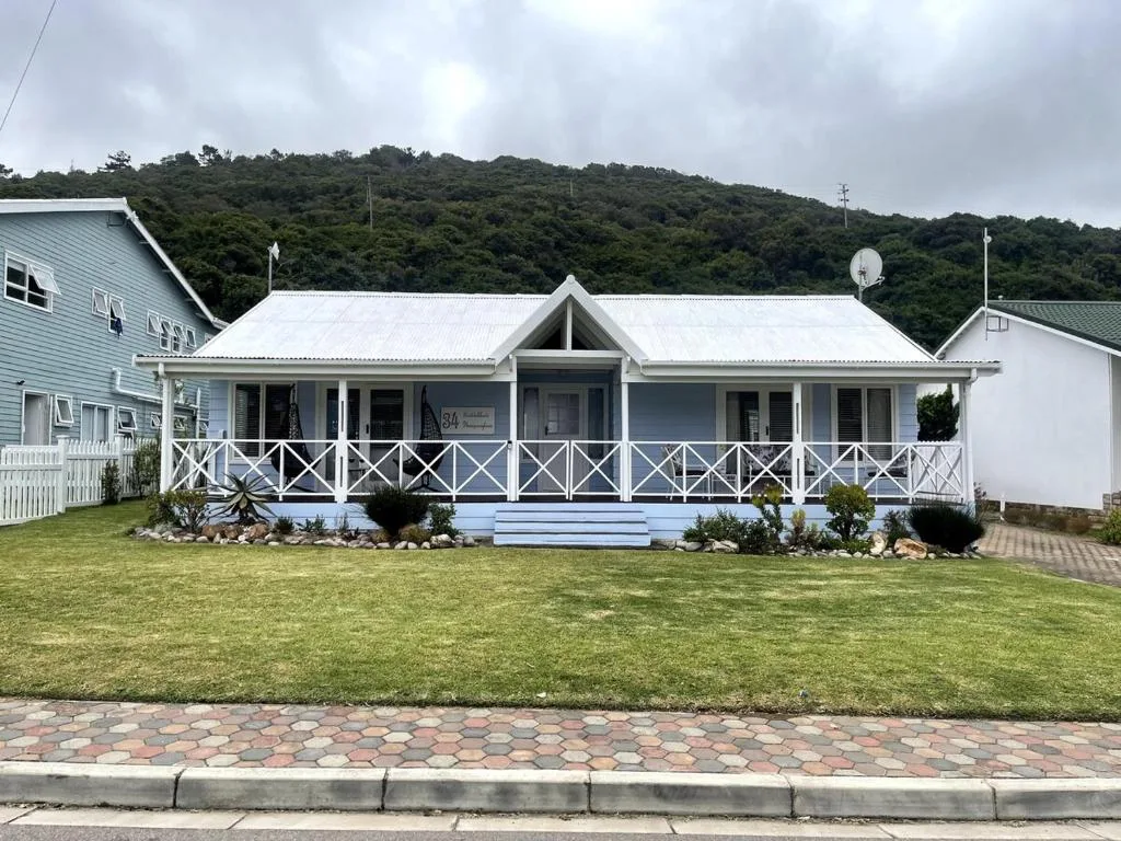 White cottage with wraparound deck and forested hillside backdrop